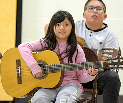 girl holding guitar looking at teacher