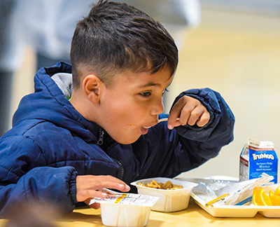 boy eating breakfast with spoon in mouth at cafeteria table