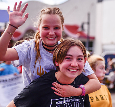 two girls walking piggy back in parade