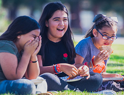 girls eating pizza on grass under a tree