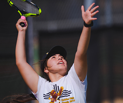 girl tossing ball up in air to serve