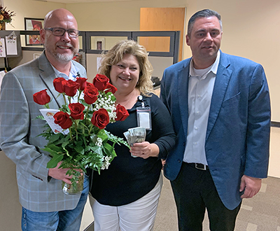 three people with flowers and cash smiling