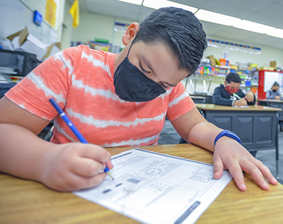 kid in mask writing a paper at desk