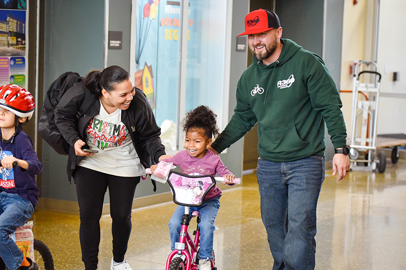 two smiling adults pushing kid on bicycle